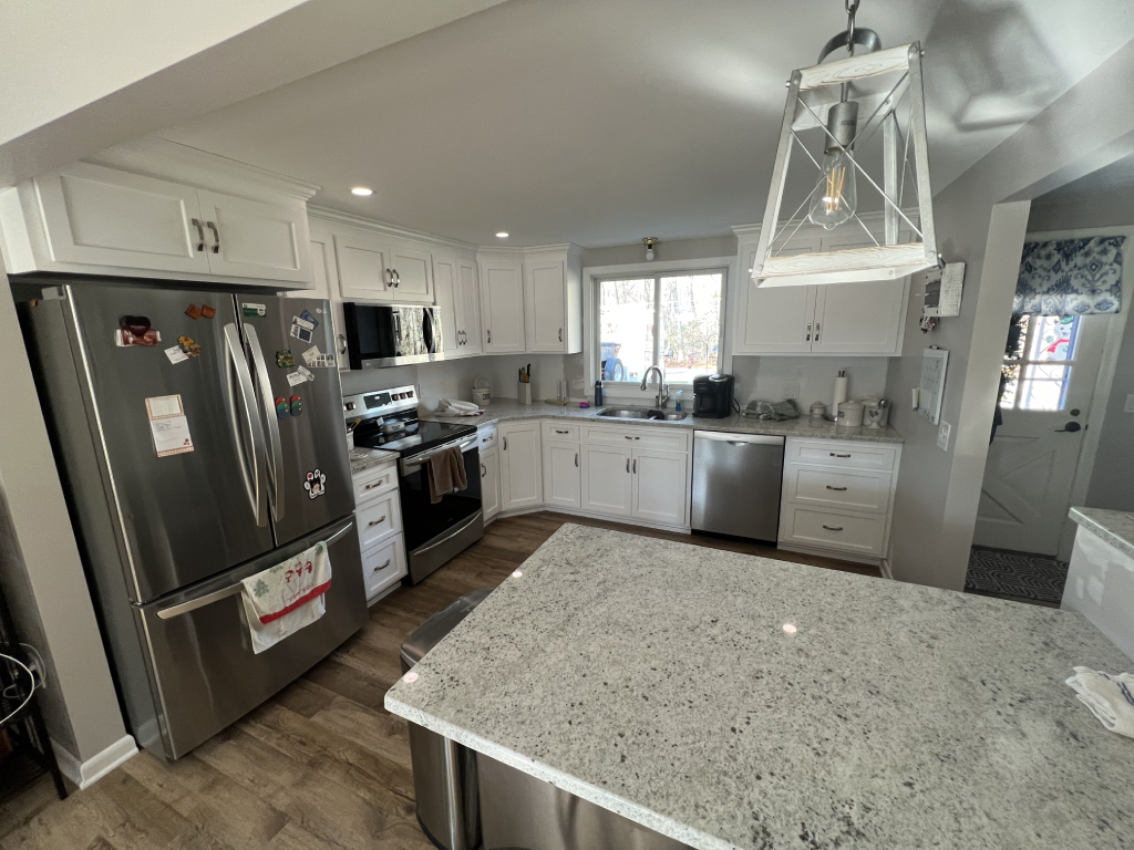 Bright modern kitchen with white cabinets, stainless steel appliances, granite island, and large window overlooking the outdoors.