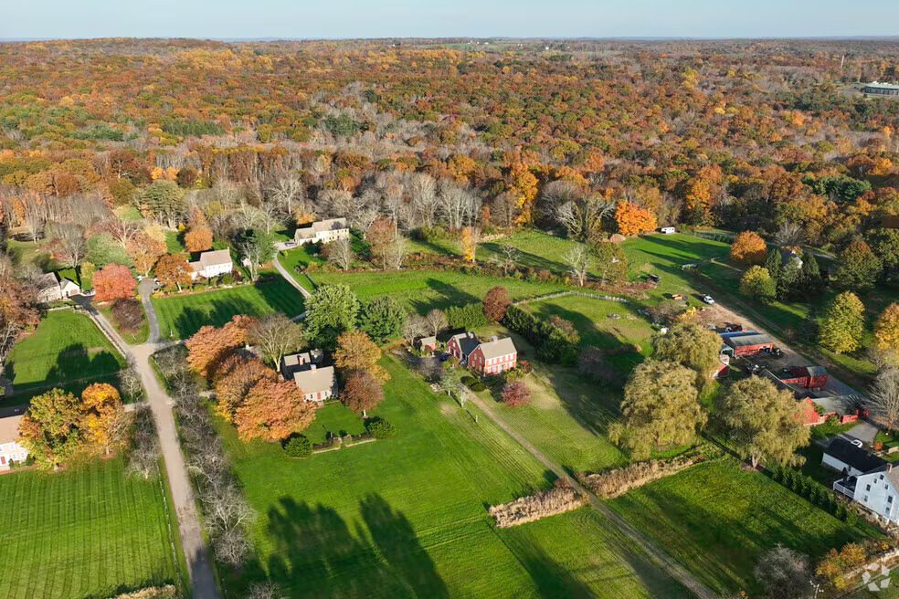 Aerial view of Hebron, Connecticut in autumn, showing scattered homes, green fields, winding roads, and dense forests with vibrant fall foliage in shades of orange, yellow, and red.